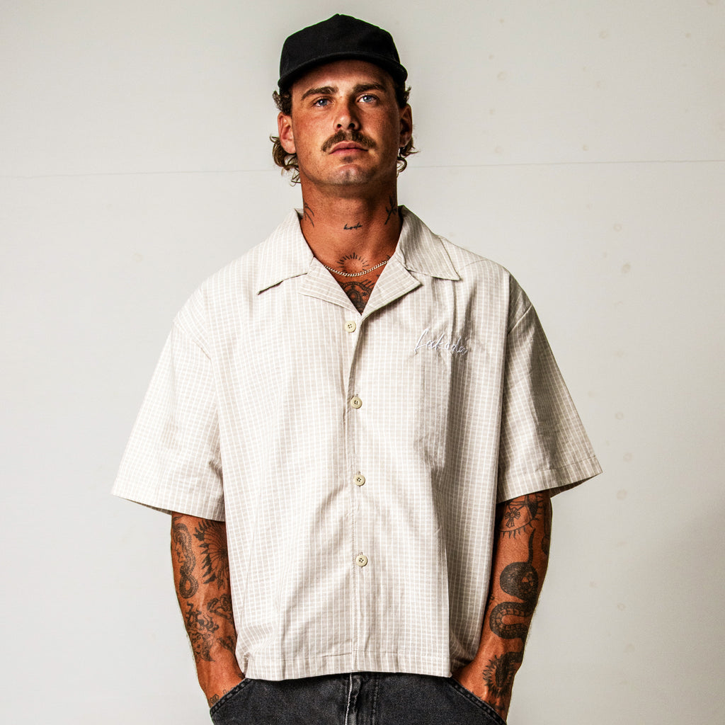 Man wearing a beige short-sleeve shirt and black cap against a plain background