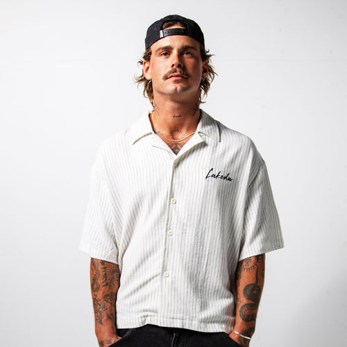 Man wearing a white striped shirt with a brand logo on a plain background