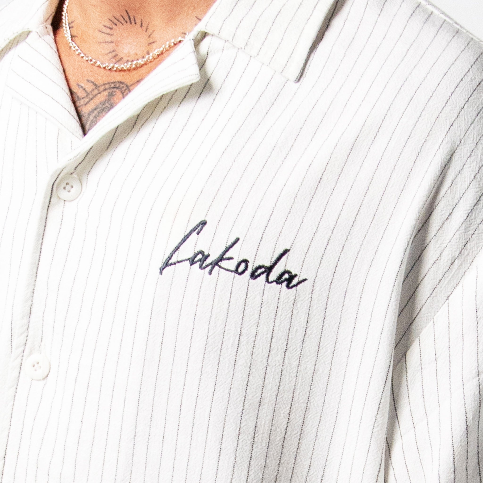 Close-up of a white shirt with 'Lakoda' embroidery on a plain background