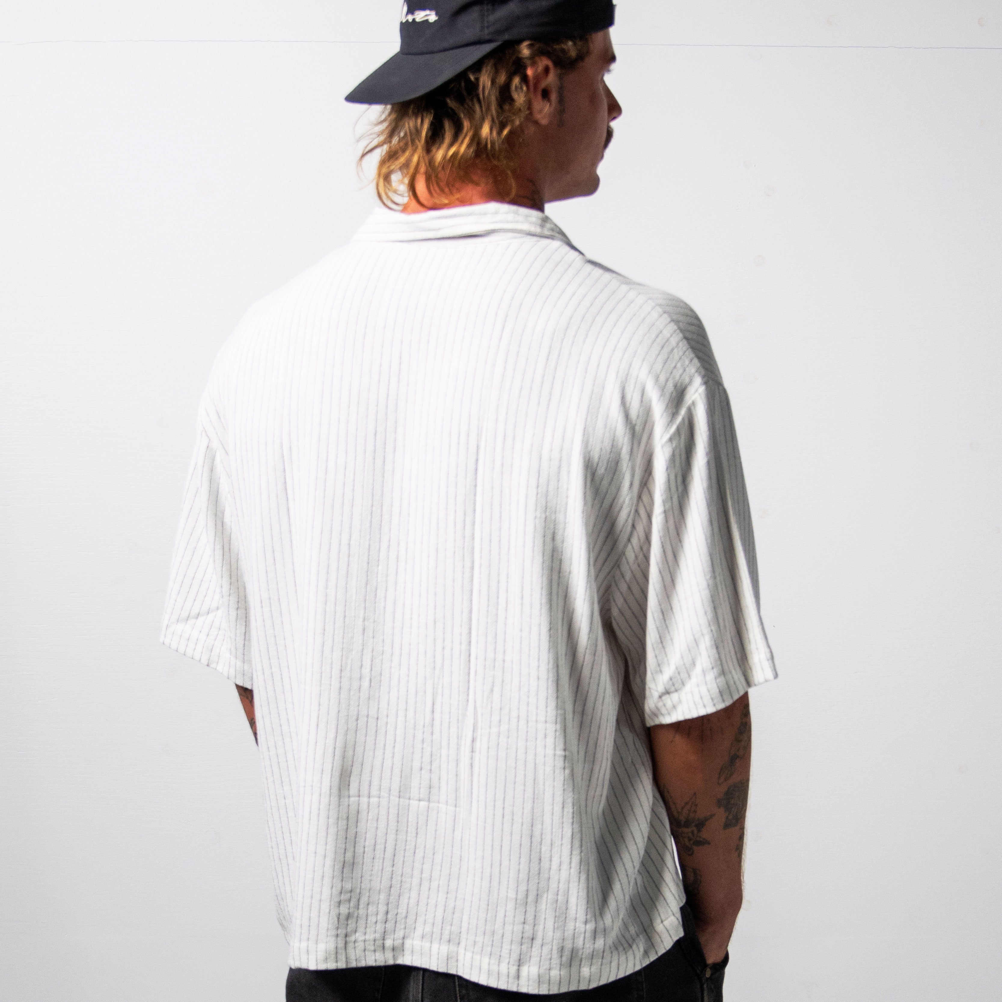 Person wearing a white button-up shirt and black cap on a plain background